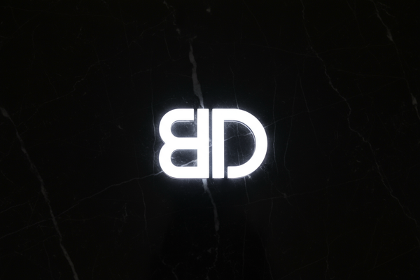 Black marble backround with the letter "B" flipped upside down at a 180 degree angle, conjoined with the letter "D" along the vertical spine of each letter, and the "D" is at a 0 degree angle in its correct position. Make the whole logo in white LED lights.